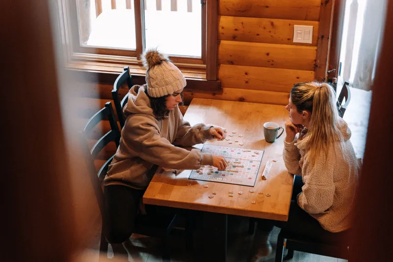 Two guests at a wooden table in a log cabin at Baker Creek, planning activities with a map and game pieces.
