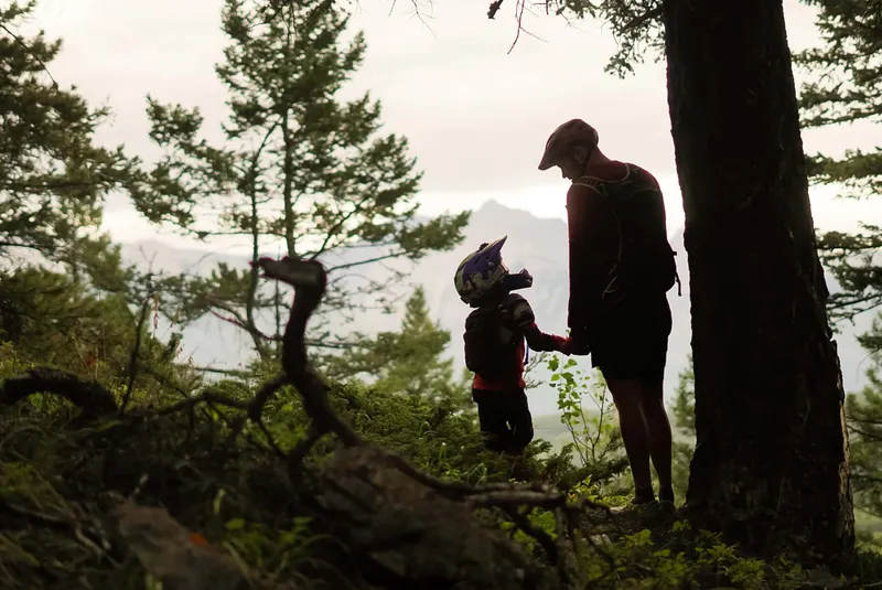Adult and child hiking on a forested trail near Buffalo Mountain Lodge with mountain views beyond.