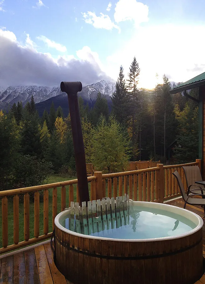 Hot tub with wood barrel surround overlooks forested valley and snow-capped peaks at Cross River.