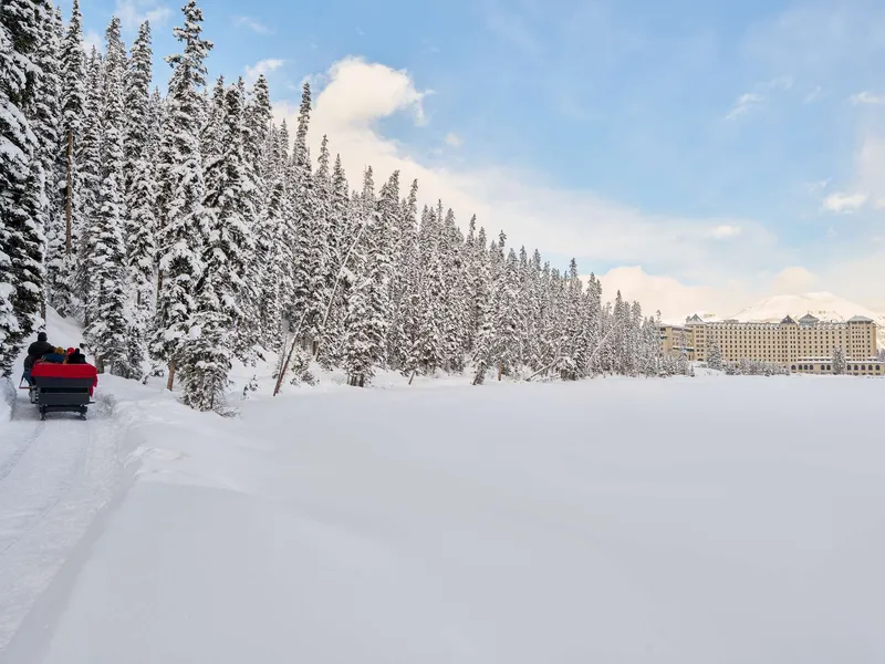Fairmont Lake Louise castle-style building rises beyond snow-covered evergreens and frozen lake surface.