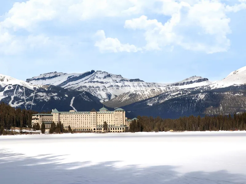 Fairmont Chateau Lake Louise stone chΓ’teau on frozen lake with snow-capped peaks beyond.