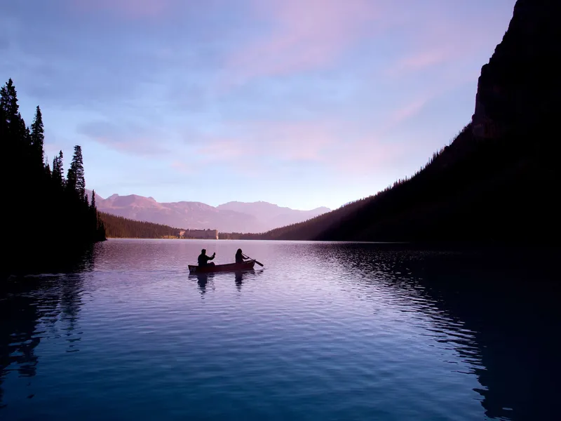 Two guests canoe on Lake Louise at dawn with Fairmont Chateau Lake Louise visible across the water.