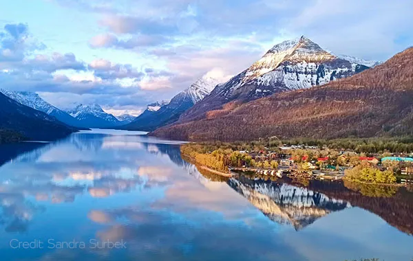 Kilmorey Lodge nestled along Waterton Lake shoreline with snow-capped peaks reflected in calm waters.