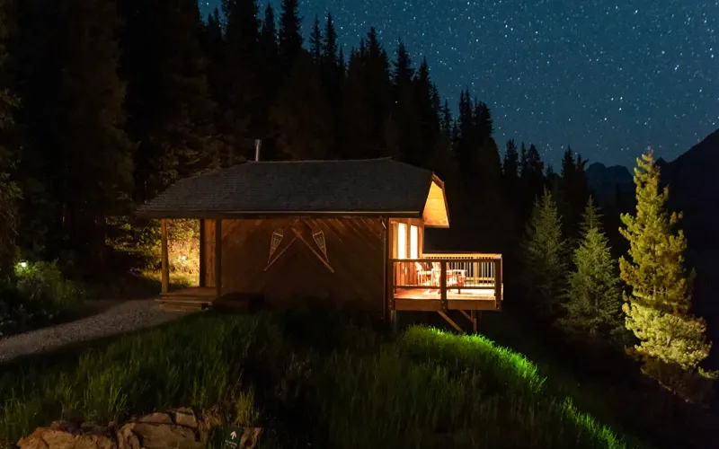 Whiskey Jack cabin at Mount Engadine Lodge glows warmly at night beneath star-filled Kananaskis skies.