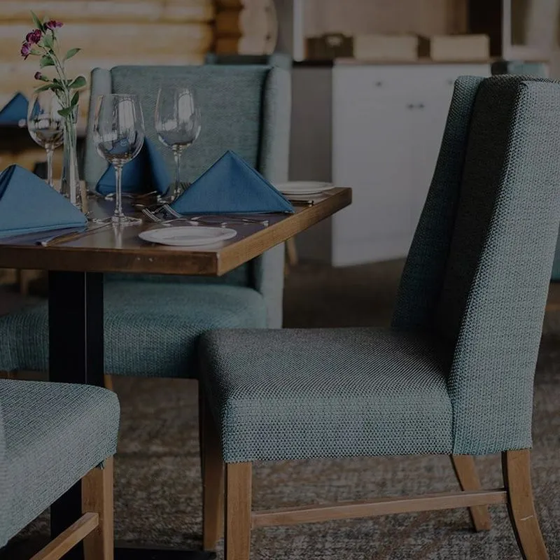 Overlander Mountain Lodge dining room with wood table, blue-upholstered chairs, and place settings with wine glasses.