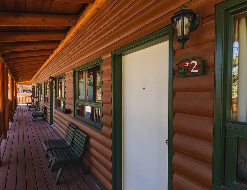 Log cabin corridor with numbered green-trimmed doors and wooden deck at Overlander Mountain Lodge.