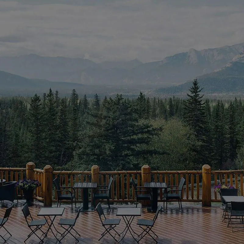 Overlander Mountain Lodge timber deck overlooks forested valley and snow-capped Jasper mountains.