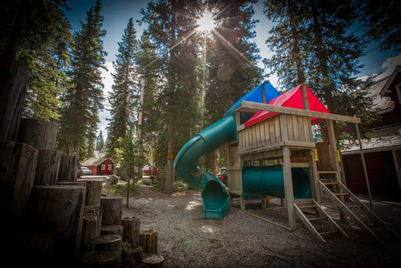 Paradise Lodge playground with wooden structures, spiral slide, and coniferous forest backdrop.