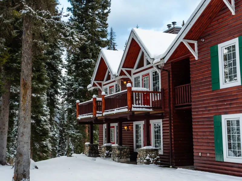 Red log cabins with pitched roofs and snow-covered decks nestle in coniferous forest at Paradise Lodge.