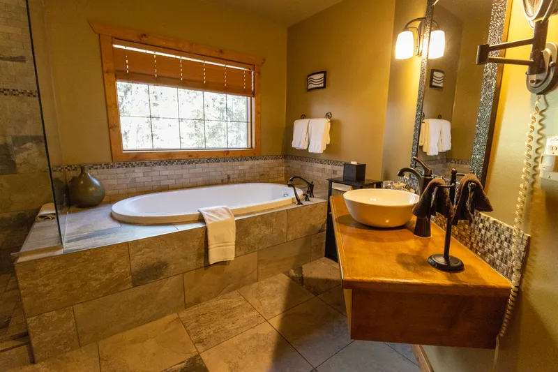 Prairie Creek Inn's treehouse bathroom with stone soaking tub, wood vanity, and forest views through window.