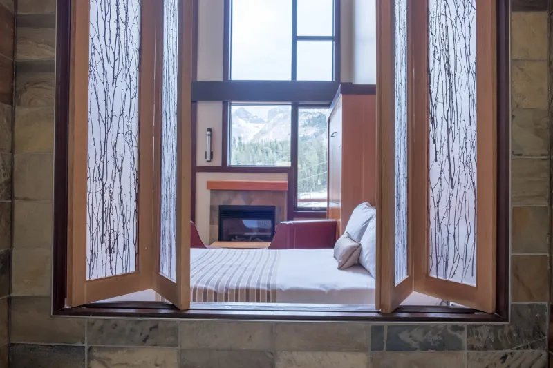 Sunshine Mountain Lodge loft bedroom with wood beams, fireplace, and mountain views through windows.