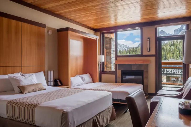 Sunshine Mountain Lodge premier room with two beds, wood ceiling, fireplace, and mountain views through windows.