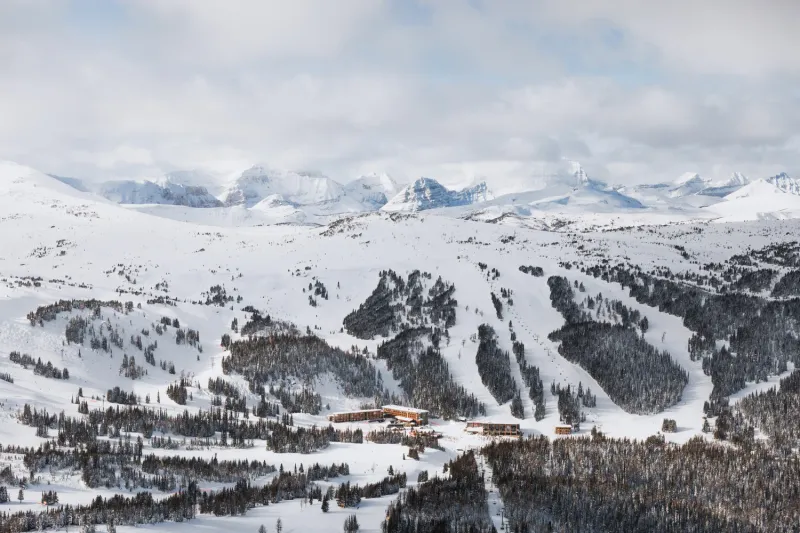 Sunshine Mountain Lodge nestled in snowy valley surrounded by forested slopes and distant peaks.
