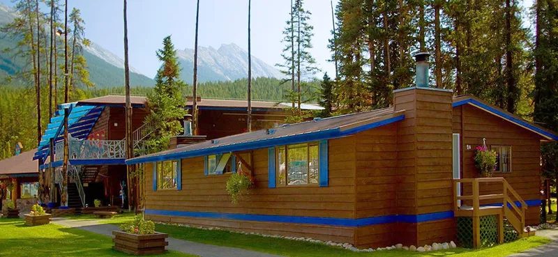 Log cabin day lodge with blue trim and wooden deck, mountains rising beyond coniferous forest at Sunwapta Falls.